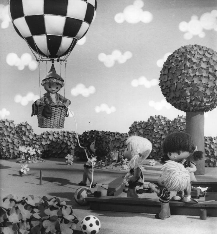 Das Sandmännchen in einem Heißluftballon. Vier Kinderfiguren beobachten es.