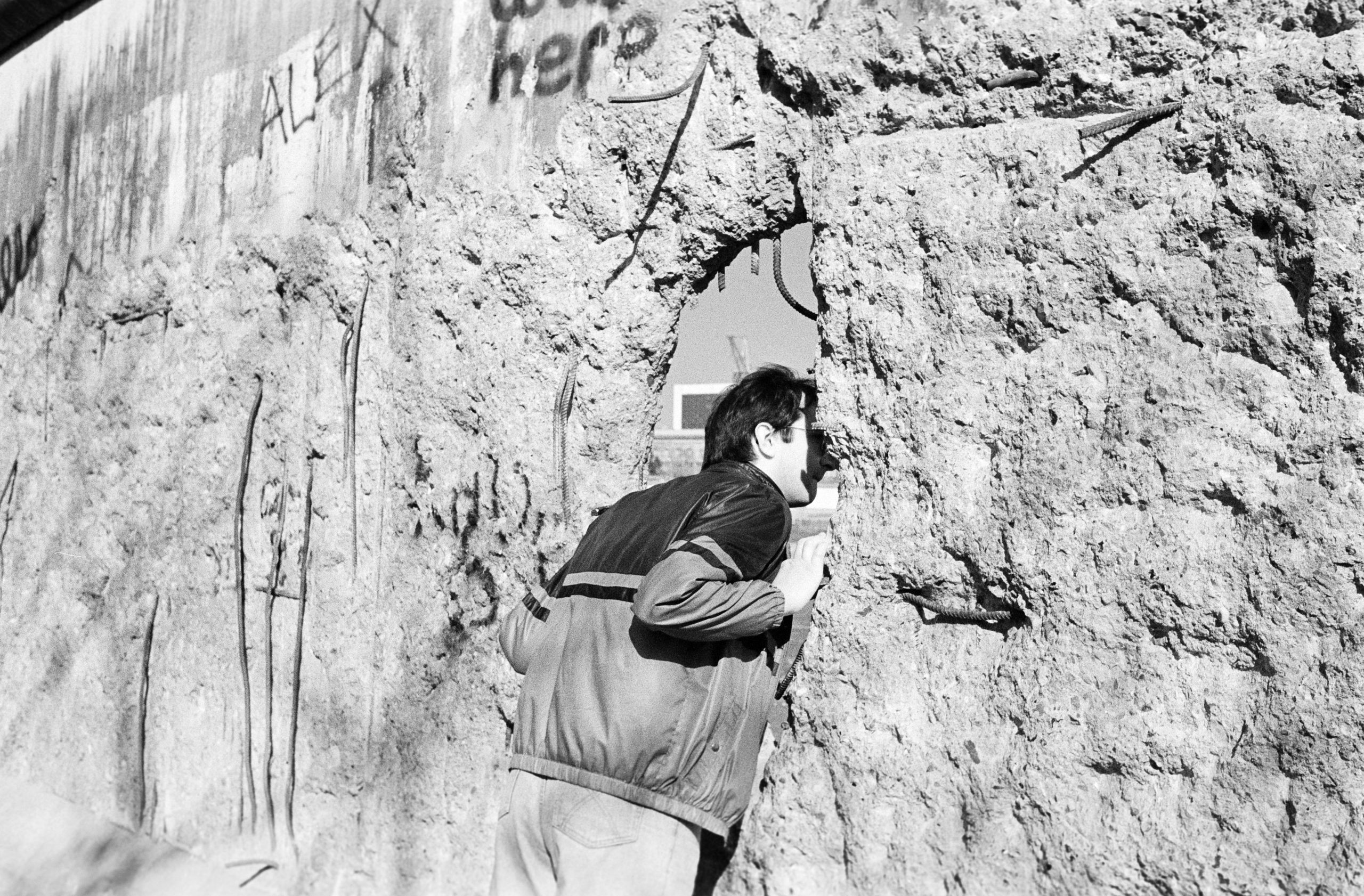 Eine Person schaut durch ein Loch in der Berliner Mauer.