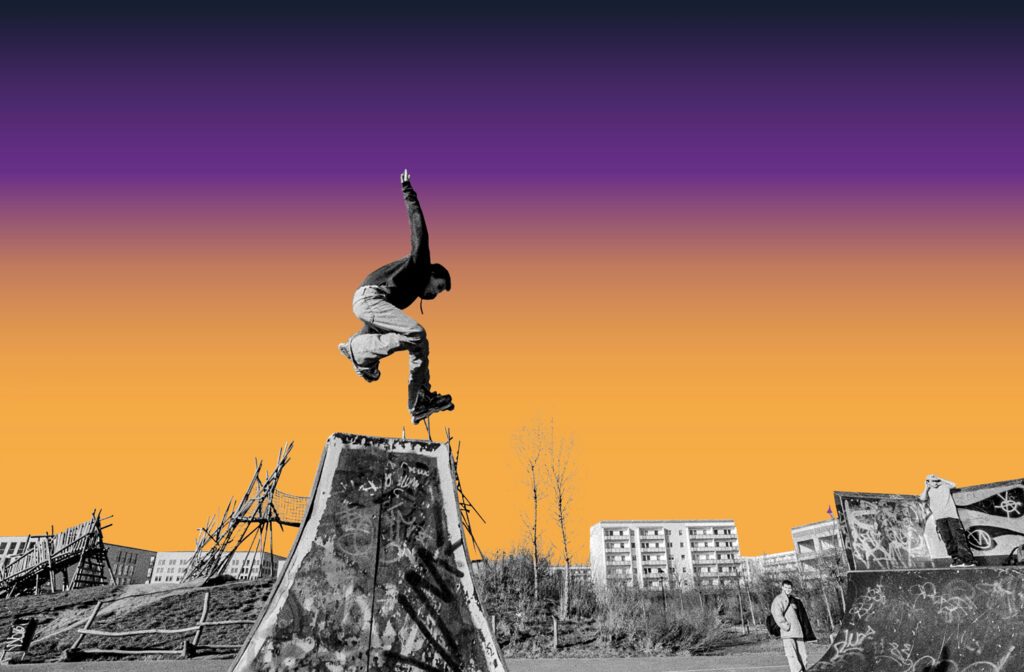 Umbruchszeitenlogo mit Bild. Ein Skater springt über den Rand einer mit Graffiti besprayten Halfpipe. Zwei andere Jungen schauen ihm zu.
